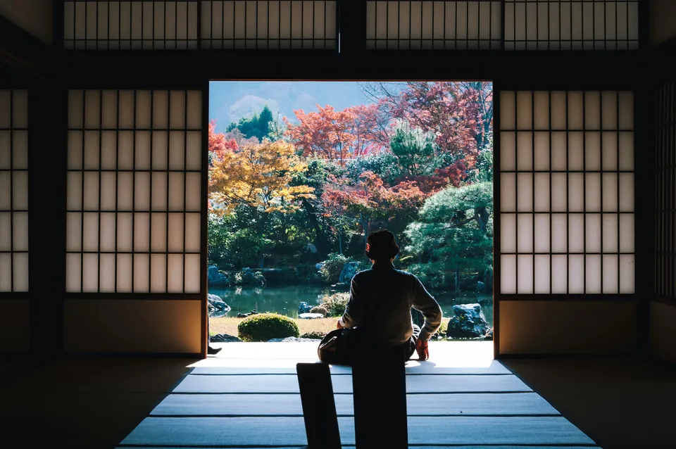 Person seated in a traditional Japanese room facing an autumn garden