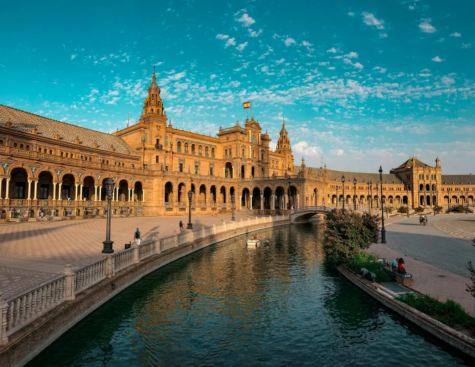 Ornate Spanish buildings beside a canal and arched bridge