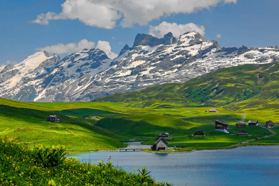Lake and green meadows beneath snow-capped Swiss mountains