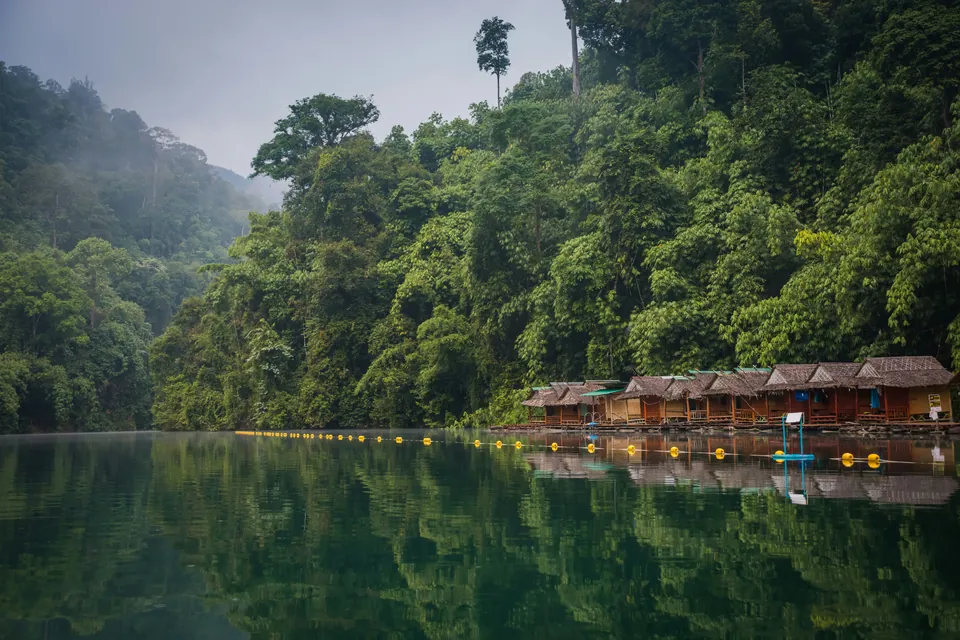 Floating cabins on a lake beside forested hills in Thailand