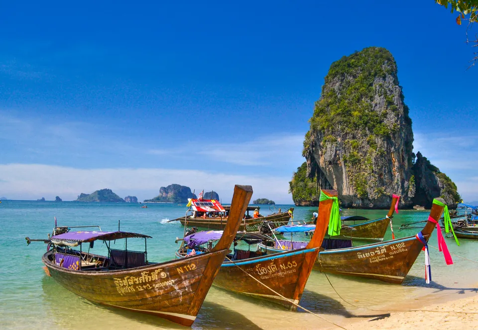 Long-tail boats beside a limestone island and sandy beach in Thailand